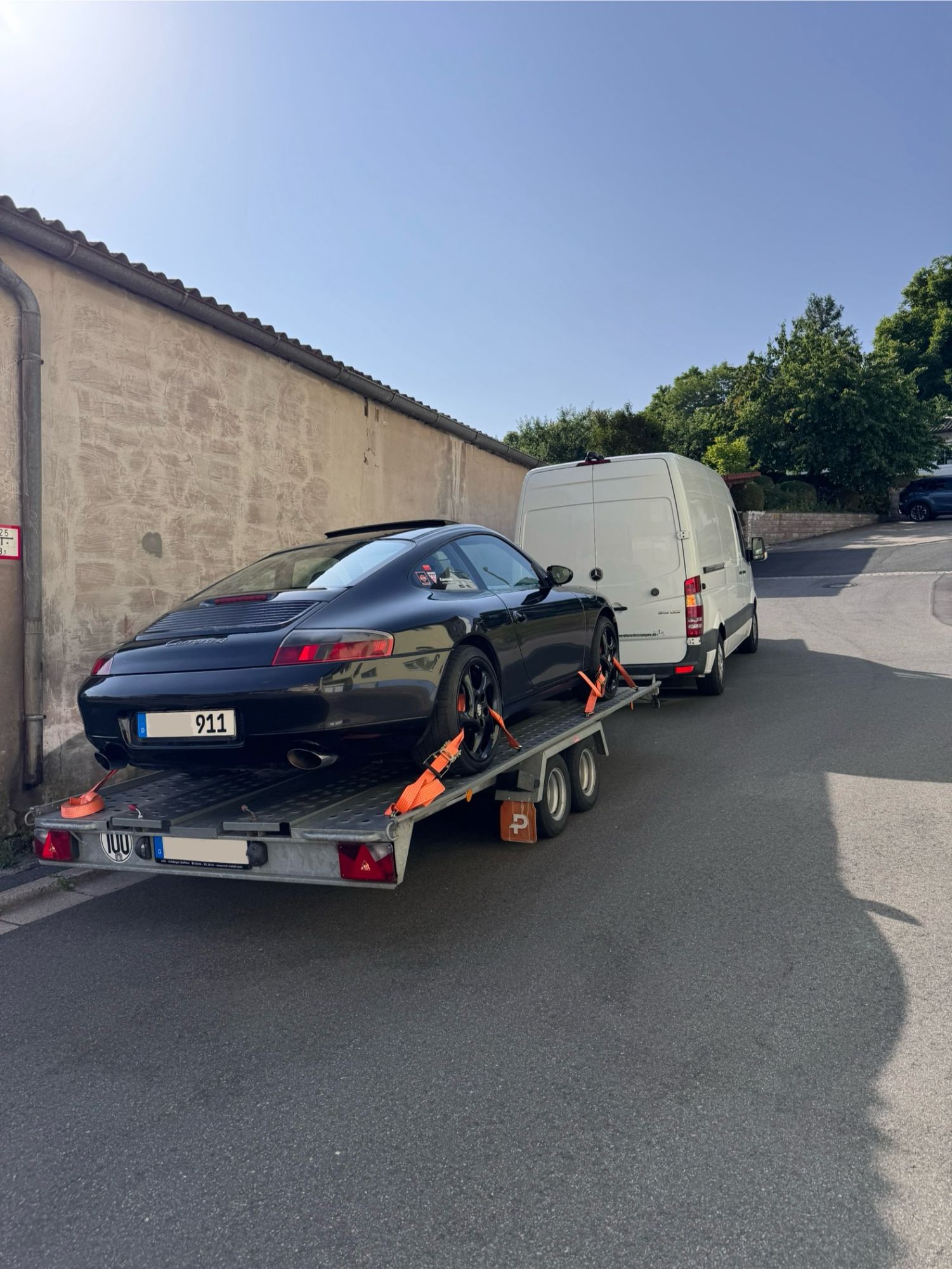 Sportwagen, mit Spanngurten auf einem Autotransport-Anhänger gesichert, hinter einem weißen Transporter