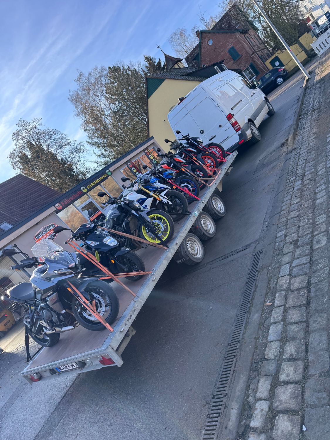Sieben festgezurrte Motorräder auf einem langen Plattformanhänger hinter einem Transporter